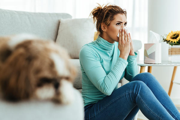 A woman sitting on the floor in front of her couch, holding a tissue up to her nose